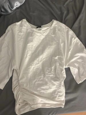 Vit topp  - Säljer en vit topp i mjukt, med rund hals och korta ärmar. Toppen har en snygg snörningsdetalj på sidan som ger en omlottkänsla och lite extra form. Perfekt till jeans eller kjol för en clean och fräsch look. Tröjan har använts två gånger. Säljer då det är för tight för mig.