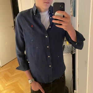 Mörkblå skjorta från Ralph Lauren - Snygg mörkblå skjorta från Ralph Lauren med klassisk button-down krage och vita knappar. Broderad röd logga på bröstet ger en clean och stilren look. Skjortan är i mjuk linne och har lång ärm, perfekt för dig som gillar tidlös stil. Nypriset ligger på 2199kr och skicket är 9/10. Priset kam diskuteras vid snabb affär🤩