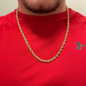 Guldtonat repkedje halsband 60 cm - Snyggt halsband med repkedje-design i guldtonad metall. Längden är 60 cm och bredden 6-7 mm, vilket ger en rejäl och stilren look. Perfekt för dig som vill ha ett statement piece som syns. Låsningen är enkel och smidig. Passar både till t-shirt och hoodie.