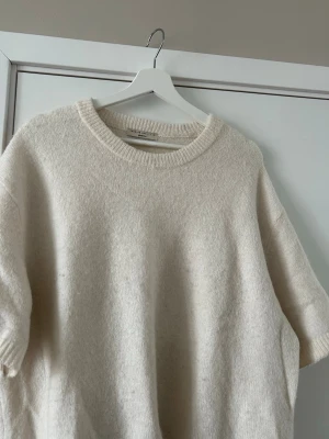 Off-White stickad kortärmad tröja - Off-White stickad tröja från Gina Tricot med korta ärmar och rund hals. Tröjan har en mjuk och lite luddig känsla tack vare mixen av ull, alpacka och syntet. Passar mig bra i storlek, är något oversized, är annars storlek medium.