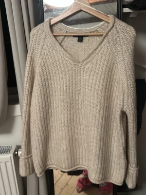 Beige stickad tröja från Amisu - Mysig beige stickad tröja från Amisu i storlek XS, dock oversize. Tröjan har v-ringning, lång ärm och en chunky ribbad struktur som ger en avslappnad vibe. Perfekt för lager på lager under kyliga dagar.