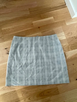 Grå rutig kortkjol - En stilren grå kortkjol med rutigt mönster. Kjolen har en klassisk rak passform och dragkedja bak