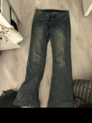 Blå bootcut jeans med tryckt patch - Säljer ett par blå jeans från Cheap Monday med bootcut-modell och klassisk femficksdesign.  Storlek 28/32