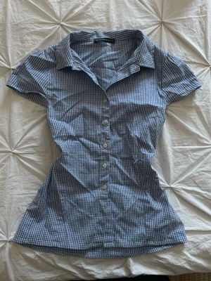 Blårutig kortärmad skjorta Brandy Melville - Supersöt blårutig skjorta från Brandy Melville med korta ärmar och figurnära passform. Skjortan har klassisk krage, knappar hela vägen och är gjord i mjuk bomull. Perfekt till jeans eller kjol för en chill look.