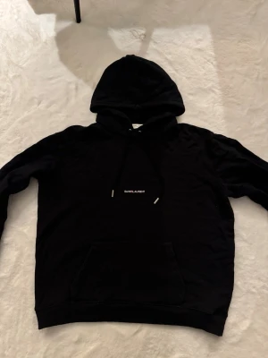 Saint Laurent hoodie  - Skick: mycket bra, inga fläckar / hål Detaljer: 	•	Färg: svart  	•	Material: bomull 	•	Passform: regular fit 	•	storlek: XL (Passar medium)  Plagget kommer från rök- och djurfritt hem.  📦 Frakt: skickas samma dag om köp går igenom innan 18.00 💬 Frågor: Hör av dig om du vill ha fler bilder eller mått 🤝 Paketpris: Samfraktar gärna vid flera köp 
