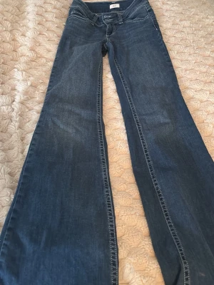 Blå bootcut jeans med broderad ficka från nelly - Säljer ett par blå jeans med bootcut passform och snyggt broderad bakficka. Jeansen har klassisk femficksdesign, låg midja och är tillverkade i slitstarkt denim. Perfekta för dig som gillar en retro och avslappnad stil.