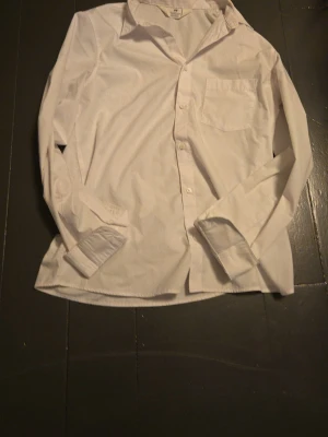 Vit skjorta från H&M, strl 164 - Klassisk vit skjorta från H&M i storlek 164. Skjortan har lång ärm, bröstficka och knäppning framtill. Perfekt till skjortstil och enkel att matcha med olika outfits. Tillverkad i mjuk bomull för skön känsla.