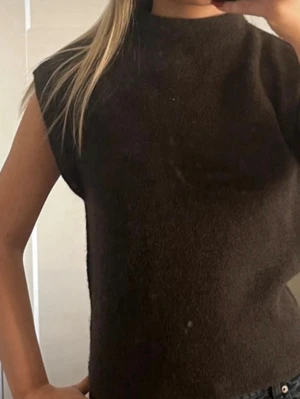 Brun ärmlös stickad tröja - Mysig brun stickad tröja utan ärmar. Tröjan har en hög hals och kommer från ginatricot!