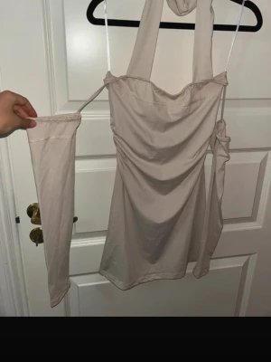 Beige offshoulder topp med långa ärmar - Trendig beige offshoulder topp med långa ärmar och bred halterneck. Toppen har en draperad front och är tillverkad i ett mjukt, stretchigt material som ger en snygg passform. Perfekt för dig som gillar stilrena plagg med en twist.