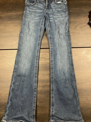 Blå bootcut jeans Gina Tricot 158 - Snygga blå bootcut jeans från Gina Tricot i storlek 158. Jeansen har klassisk femficksdesign, dekorativa bakfickor med knapp och lätt slitna detaljer för en cool look. Tillverkade i mjukt denimtyg som sitter skönt hela dagen.