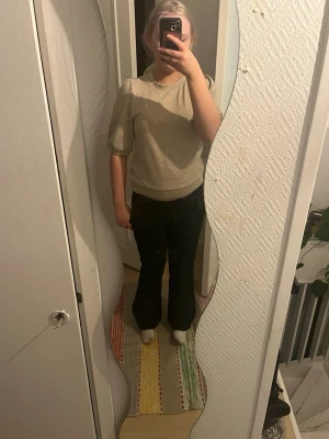 Beige stickad topp med puffärm - Säljer en beige stickad topp med puffiga, korta ärmar och rund halsringning. Toppen har en mjuk och lite glansig yta som ger en stilren look. Perfekt att matcha med både jeans och kjol för en trendig vibe.