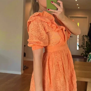 Orange kort klänning med volang - Superfin persikofärgad / orange  kortklänning med broderade detaljer och volanger längs v-ringningen. Puffiga korta ärmar och markerad midja.  Säljer för jag har två likadana!💕
