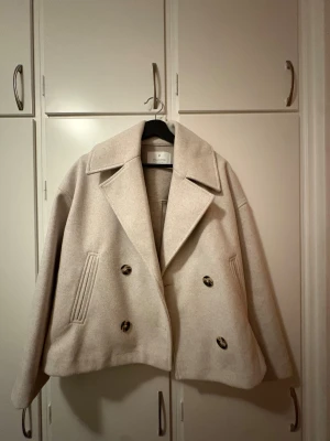 Beige jacka Stradivarius - Säljer en beige skepparkavaj från Stradivarius med bred krage och dubbelknäppning. Jackan har en loose passform, långa ärmar och är tillverkad i mjuk ullmix. Snygga knappar framtill och stilrena fickor på sidorna. Perfekt för höst och vår. Använd 2 gånger.