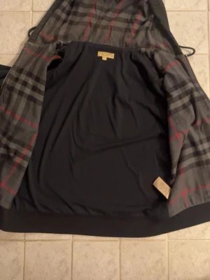 Svart burberry zip up hoodie - Svart hoodie från Burberry i storlek M med dragkedja och klassiskt rutigt foder i huvan. Två stora fickor framtill och guldfärgad dragkedja. Materialet är mjukt och skönt bomullstyg. Perfekt för dig som gillar stilrena och exklusiva plagg och har några defekter som ni kan se på bild 3 där det förekommer färgstänk men det går säkert bort med att gnugga med lite sprit men annars riktigt najs hoodie med stor luva! Det är bara att skriva om ni undrar något!☺️☺️☺️🤝👍