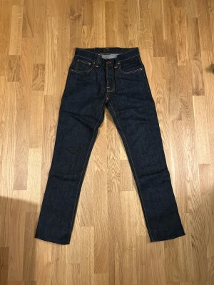 Mörkblå jeans från Nudie Jeans Co - Snygga mörkblå jeans från Nudie Jeans Co med klassisk femficksdesign och kontrastsömmar. Modellen har rak passform och är tillverkad i ekologisk bomull. Perfekt för dig som gillar stilrena och tidlösa jeans med coola detaljer.