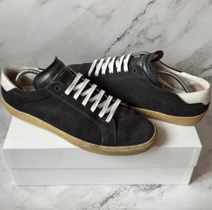 Svarta Saint Laurent sneakers  - Snygga svarta sneakers från Saint Laurent i mjuk mocka med vit häl och nya vita snören. Platt beige sula och svart läderdetalj på plösen. Grå snören + dustbag ingår