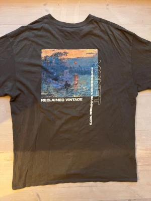 Mörkgrå Monet t-shirt Reclaimed Vintage strl L - Mörkgrå graphic tee från reclaimed vintage i storlek L. Tryck på ryggen med motiv från Monet