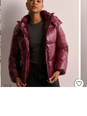Vinröd glansig pufferjacka från Nelly - Säljer en vinröd pufferjacka från Nelly med glansig finish och huva. Jackan har dragkedja framtill, hög krage och quiltad design. Perfekt för kalla dagar och ger en cool vibe till din outfit.