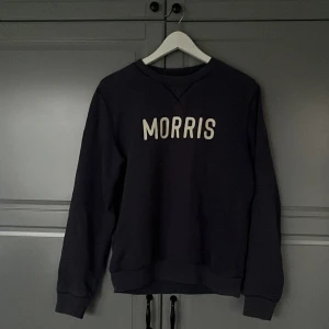 Svart sweatshirt från Morris - Säljer en stilren mörkblå sweatshirt från Morris med texten 'MORRIS' i vitt på bröstet. Tröjan har långa ärmar och en klassisk rund halsringning. Perfekt för en avslappnad look. Skick 9/10 knappast använd hör av er vid frågor och pris går att diskutera//Calle