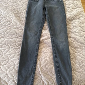 Grå skinny jeans från True Religion - Säljer ett par grå skinny jeans från True Religion med klassiska broderade bakfickor och snygga detaljer på fickorna fram. Jeansen har normal passform och är tillverkade i mjukt denim-material. Perfekt för dig som gillar stilrena och coola jeans.