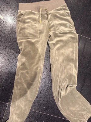 Gröna Juicy byxor i sammet - Säljer ett par gröna mjukisbyxor från Juicy Couture i mjuk sammet. Byxorna har bred resår i midjan med gulddetaljer på snöret, stora fickor fram och broderad logga på vänster sida. Perfekta för chill dagar och riktigt sköna att ha på sig.