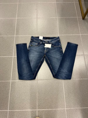 Blå slimmade  jeans från Tiger of sweden W30 L34 - Snygga blå jeans från T/J med smal passform och smal fot. Klassisk femficksdesign, bruna detaljer och läderpatch bak. Jeansen har en mörk tvätt med lätt slitning och är tillverkade i jeansmaterial. Perfekta för dig som gillar en slim look.