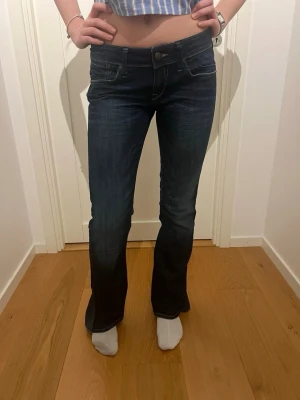 Mörkblå lågmidjade bootcut jeans - Snygga mörkblå jeans med bootcut passform och klassiska fickor fram och bak. Jeansen har en lätt tvättad look och sitter skönt i midjan. Perfekta för dig som gillar en tidlös stil med lite utsvängda ben. Materialet är klassisk denim. Storleken på dessa jeans är S