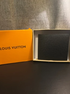 Svart plånbok - Snygg svart plånbok i exklusivt präglat skinn. Klassisk fyrkantig form med logga diskret i hörnet. Plånboken har flera kortfack och fönster för ID, perfekt för dig som vill ha stil och funktion i ett.