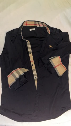 Svart burberry skjorta  - Hej säljer den jätte fin svart burberry skjorta med rutiga armar man kan veckla upp och finns även på insidan av kragen vid halsen. Den är använde mellan 2-5 gånger i somras å är i jätte bra skick å singa skador. Det står L men sitter jätte bra som M. Om ni undrar någon är det bara och skriva. Pris kan diskuteras