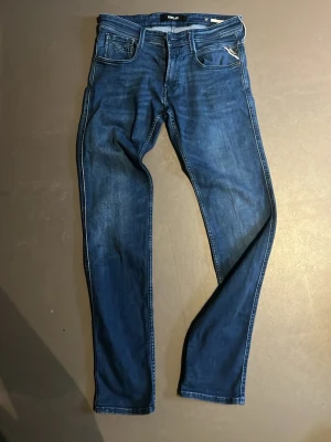 Replay Anbass jeans blå, storlek 29 - Snygga Replay Anbass jeans i mörkblå tvätt med klassisk femficksdesign och diskreta slitningar. Perfekta för dig som gillar stilrena jeans med modern look.