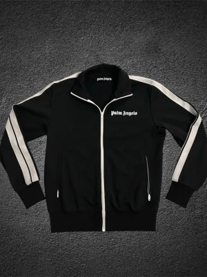 Palm angels tracksuit jacka  - Säljer denna feta Palm angels tracksuit jackan! | skicket är 10/10 då den knappt blivit använd | Storlek M | självklart är den helt äkta (se bild 5) | skriv vid minsta fundering! | skickar inom 24h📦| säljer denna till ett extremt bra pris då de oftast säljs äkta för 3000kr och upp. 