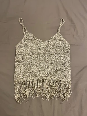 Stickad linnetopp med fransar från MNG - Säljer en beige och vit stickad linnetopp från MNG i storlek XS. Toppen har smala axelband, ett snyggt mönster med öppna partier och långa fransar längs nederkanten. Perfekt för sommarens chillaste dagar och festivaler. Knappt använd. 