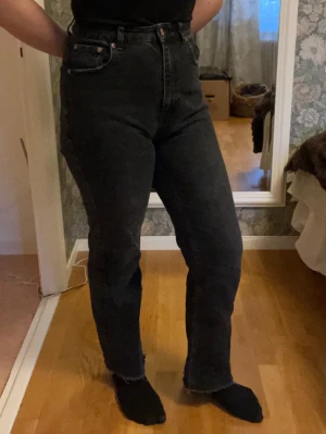 Svarta raka jeans från NA-KD - Säljer ett par svarta jeans från NA-KD med hög midja och raka ben. Jeansen har klassisk femficksdesign, kopparfärgade nitar och rå kant nedtill för en edgy vibe. Materialet är robust denim i bomull. Perfekta för dig som gillar en clean och stilren look.
