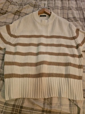 Randig stickad tröja från Gina Tricot - Säljer en chunky stickad tröja från Gina Tricot i storlek M. Tröjan är vit med bruna ränder, har ribbade muddar och en rund halsringning. Perfekt för lager-på-lager och chill höst- och vinterdagar.