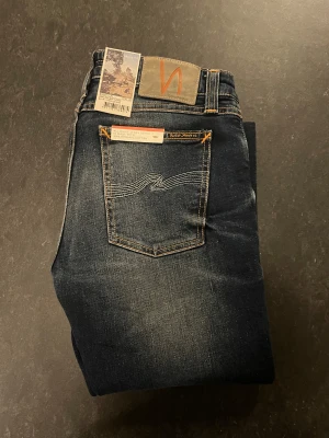 Nudie Jeans Skinny Lin mörkblå jeans - Säljer ett par snygga mörkblå Skinny Lin jeans från Nudie Jeans och med storleken W30/L32. Modellen är skinny fit och är bekväma där de är lite stretchiga. Mycket fint skick där de är helt nya med prislapp. 1399kr nypris. Säljer dessa jeans för de var för små för min storlek. Fråga gärna om det är något.