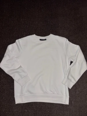 Peak Performance sweatshirt - Säljer en stilren vit sweatshirt från Peak Performance med diskret broderad logga på bröstet. Tröjan har rund hals, långa ärmar och är tillverkad i mjuk bomullsmix. Perfekt för en clean och enkel look. Mycket bra skick och endast använd ett par gånger. Så nära nyskick man kan komma. Storlek Large.