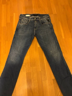 Replay Anbass jeans blå  - Snygga Replay Anbass jeans i klassisk blå tvätt med coola slitningar och ljusare partier. Modellen har raka ben och fem fickor, med kontrastsömmar på bakfickorna. Tillverkade i mjukt stretchigt jeansmaterial för skön passform. Finns en defekt se på sista bilden