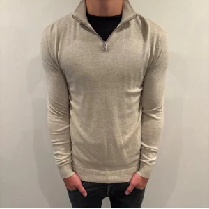 Beige stickad half zip från Jack & Jones - Snygg beige stickad tröja från Jack & Jones med kvartslång dragkedja och hög krage. Tröjan har långärmad passform och ribbade muddar vid ärmslut och nederkant. Perfekt för dig som gillar stilrena och enkla plagg. Nypris 499kr säljs för 329kr. Skick 10/10 aldrig använd. 