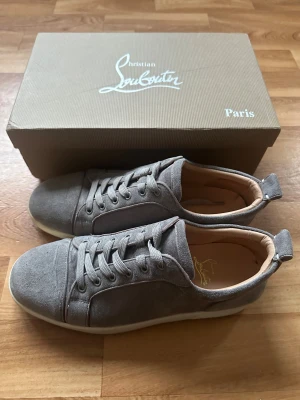 Christian Louboutins Gråa - Säljer ett par Christian Louboutins i grått. Använda men i bra skick. Medföljer originalbox, dustbag, kvitto och alla kort som kom med vid köp. Stilrena och sköna sneakers med klassiska röda sulan – perfekta för dig som vill ha ett par Louboutins till ett bra pris. Kan passa 42 också.