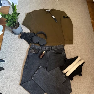 Olivgrön sweatshirt från Stone Island - Snygg olivgrön sweatshirt från Stone Island med klassisk patch på vänster ärm. Tröjan har rund hals, långa ärmar och ribbade muddar. Tillverkad i mjuk bomull som är skön mot huden. Perfekt för dig som gillar streetwear och vill ha en clean look. 