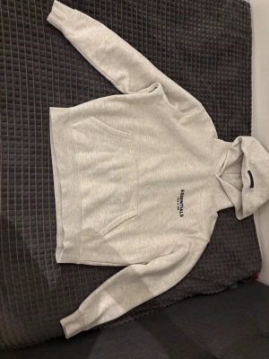 Grå Essentials Fear of God hoodie - PRIS KAN DISKUTERAS!! Snygg ljusgrå hoodie från Fear of God Essentials med svart tryck både fram och bak. Klassisk känguruficka, ribbade muddar och stor huva. Tillverkad i mjuk bomullsblandning som känns riktigt skön mot huden. Perfekt för dig som gillar streetwear och clean stil.