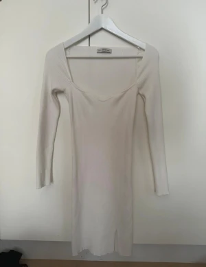 Vit ribbad långklänning från Chiquelle - Supersnygg vit långklänning från chiquelle med ribbad struktur och långärmade smala ärmar. Klänningen har en djup fyrkantig ringning och en liten slits framtill för extra vibe. Perfekt för dig som gillar minimalistisk stil med en touch av edge.