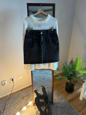 Svart jeanskjol med nitar från VILA - Cool svart jeanskjol från VILA med klassisk femficksdesign och silverfärgade nitar vid fickorna. Kjolen har en rak, kort passform och stängs med knapp och dragkedja framtill. Perfekt att styla med boots och stickad tröja för en chill look.