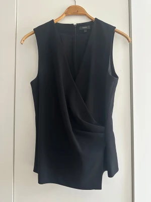 Svart omlottopp från Theory - Snygg svart omlottopp från Theory i stilren design. Toppen är ärmlös med v-ringad omlottfront och har en diskret dragkedja bak. Materialet är mjukt och har ett elegant fall