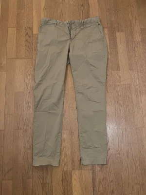 Beige chinos från J.Lindeberg 32/32 - Snygga beige chinos från J.Lindeberg i klassisk rak modell. Byxorna har två sidofickor fram och två bakfickor med knapp, samt hällor för bälte. Tillverkade i bomull för en skön och stilren känsla.