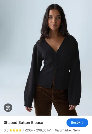 Svart blus med knappar från Nelly - Snygg svart blus med V-ringning och formad siluett. Blusen har långa, vida ärmar och knäppning framtill med små svarta knappar. Endast använd 1 gång.