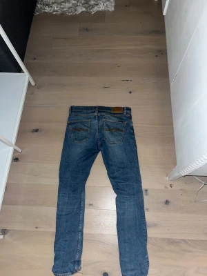 Blå Nudie Jeans W28 L30 skinny fit - Säljer ett par klassiska blå jeans från Nudie Jeans i storlek W28 L30. De har skinny fit, fyra  fickor och snygga kontrastsömmar. Perfekta för dig som gillar en smalare siluett och vill ha ett par jeans som funkar till allt. Jag säljer dom för att dom var förstora för mig 