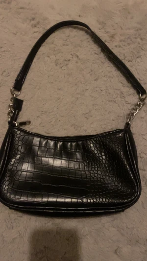 Axelväska i skinn - En axelväska i skinn och silvriga kedjor, Den är perfekt storlek då den inte är för liten eller för stor. Den är köpt från glitter.