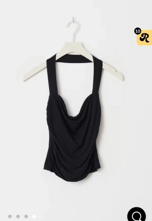 Svart halterneck topp med drapering - Snygg svart halterneck topp med draperad framsida och öppen rygg. Toppen är tight och croppad, perfekt att styla med jeans eller kjol. Tillverkad i mjukt och stretchigt material som sitter skönt mot kroppen.