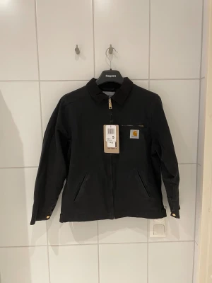 Svart Carhartt jacka - Svart Carhartt jacka som är helt oanvänd. Köpt på Naturkompaniet i våras men glömde helt att använda den så för helst tillbaka en del av pengarna så man kan droppa på lite annat. Riktigt skönt starkt material med skön insida. Carhartts klassiska tjocka dragkedja och guldknappar. Sitter riktigt bra på modellen som är 179 65kg. Skickar eller möts i Stockholm. 